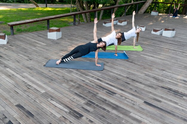 Tre giovani ragazze che fanno yoga nel parco Le ragazze fitness eseguono il super esercizio della tavola laterale all'aperto