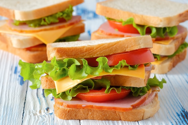 Tre gustosi panini con prosciutto, insalata, formaggio e pomodori sul tavolo in legno rustico