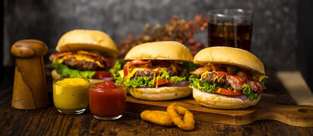 Tre hamburger con hamburger di manzo, cipolle fritte, spinaci, ketchup, pepe e formaggio serviti su una tavola di legno con bibita analcolica.