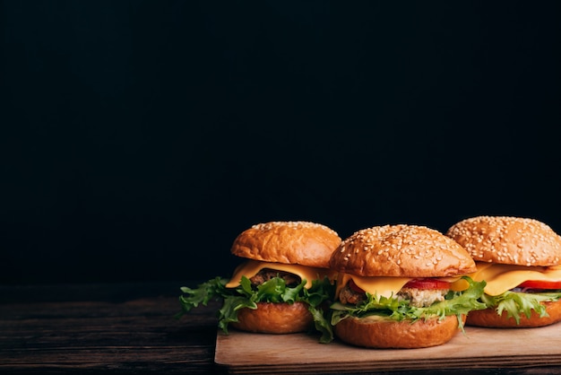 Tre hamburger fatti in casa con carne, formaggio, lattuga, pomodoro su un tavolo di legno