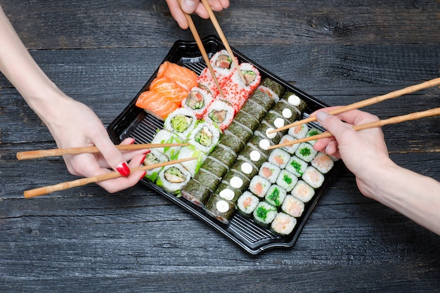 Tre mani con bacchette e set di sushi.