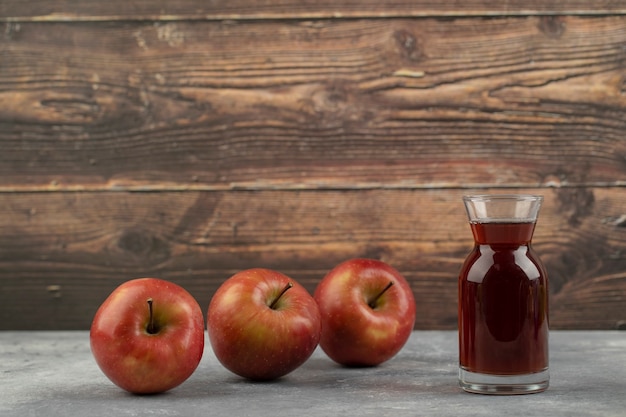 Tre mele rosse e un bicchiere di succo sulla superficie in marmo.