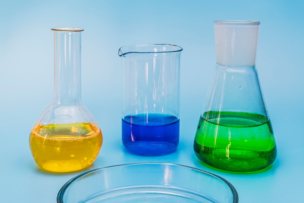 Tre palloni da laboratorio in vetro con soluzioni di giallo, verde e blu su uno sfondo medico blu delicato. Il concetto di esperimenti e ricerche mediche e chimiche. Avvicinamento. copia spazio.