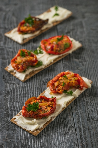 Tre pane tostato con crema di formaggio e pomodori secchi su un tavolo di legno. Spuntino vegetariano di ricotta e pomodori.