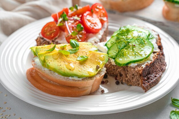 Tre panini con formaggio feta avocado pomodorini e cetriolo in un piatto bianco Vista laterale primo piano Spuntini sani