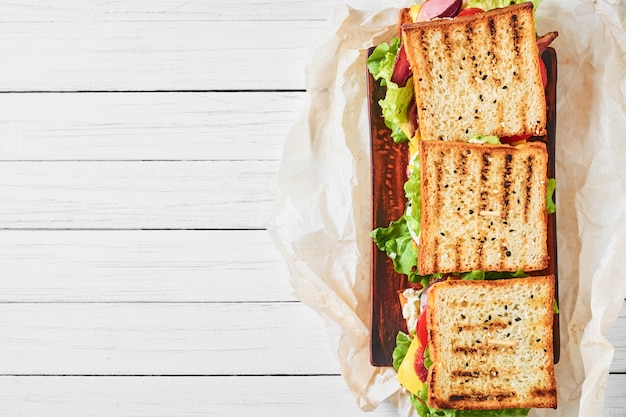 Tre panini con prosciutto, lattuga e verdure fresche su sfondo bianco, vista dall&#39;alto