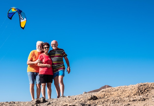 Tre persone caucasiche senior che sorridono di felicità Godendo del tempo libero e della pensione Cielo blu e kitesurf Montagna arida