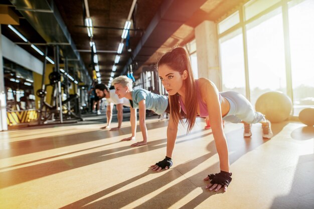 Tre persone forti che lavorano in una palestra. Fare flessioni in linea.