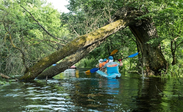 tre persone in kayak sulla canoa blu sul fiume sotto un vecchio albero caduto