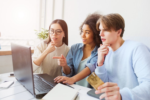 Tre persone sono stupite. Stanno guardando lo schermo dei laptop. Guy è in possesso di una carta di credito.