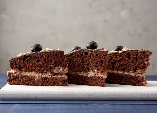 Tre pezzi triangolari di torta al biscotto al cioccolato con crema al burro su una tavola di legno bianca