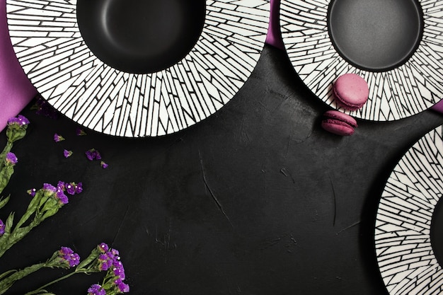 Tre piatti fantasia su sfondo nero. Impostazione creativa della tavola del ristorante con fiori e accenti di colore viola