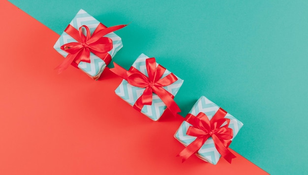 Tre piccole scatole regalo a strisce con nastri a fiocco giacciono diagonalmente su uno sfondo verde e rosso