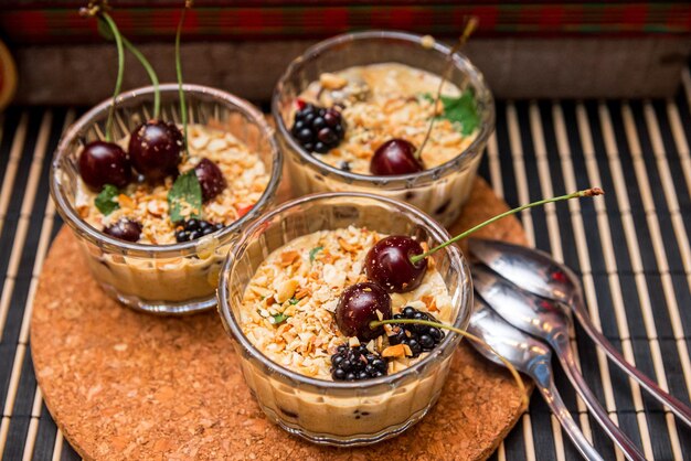 Tre porzioni di dessert alla crema alla vaniglia con arachidi tritate e more e ciliegie fresche