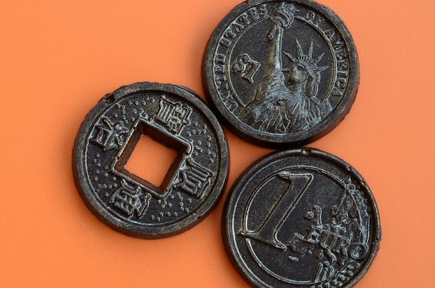 Tre prodotti di cioccolata sotto forma di monete Euro, USA e Giappone giacciono su una plastica arancione