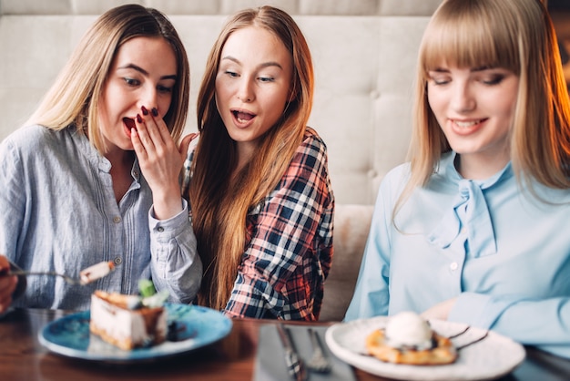 Tre pulcini sorridenti mangia torte dolci nella caffetteria. Dessert al cioccolato e alcol sul tavolo