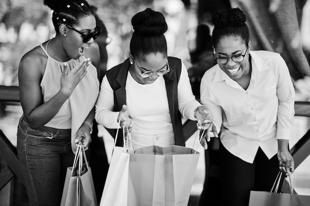 Tre ragazze afroamericane casual con borse della spesa colorate che camminano all'aperto Shopping da donna nera alla moda
