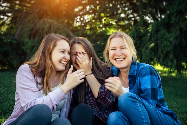 Tre ragazze allegre sussurrano e si divertono contro il fogliame verde nel parco.