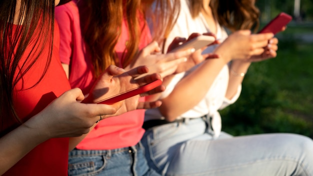 Tre ragazze che chiacchierano con i loro smartphone al parco gen z amiche che usano gadget e