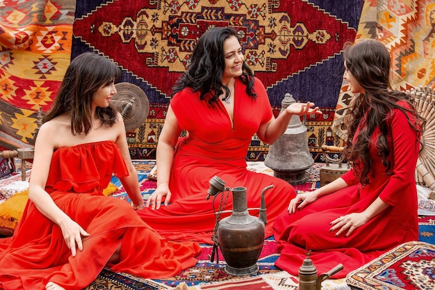 Tre ragazze in abiti rossi si siedono su tappeti turchi e parlano. Cappadocia .Turchia