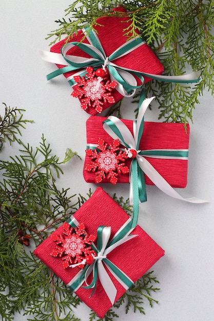 Tre regali di Natale in carta rossa con fiocchi di neve e nastri sulla superficie chiara. Regali per le vacanze di Natale Formato verticale. Vista dall'alto