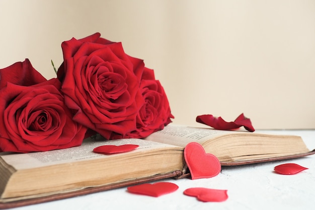 Tre rose rosse su un vecchio libro aperto su un tavolo e molti cuori rossi.