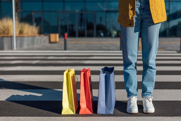 Tre sacchetti di carta per lo shopping e una donna in piedi sulle strisce pedonali contrassegnate