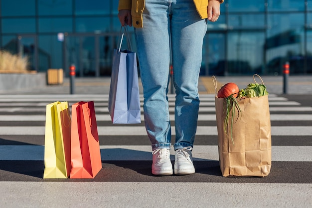 Tre sacchetti di carta per lo shopping e una donna in piedi sulle strisce pedonali contrassegnate