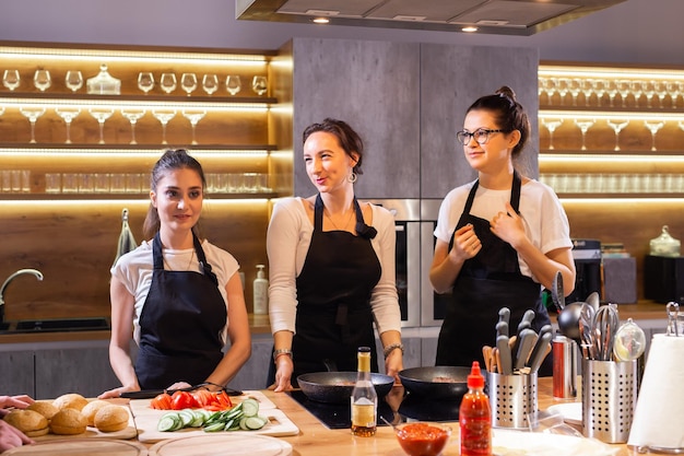 Tre simpatiche chef professioniste che preparano il cibo nella grande cucina e si divertono