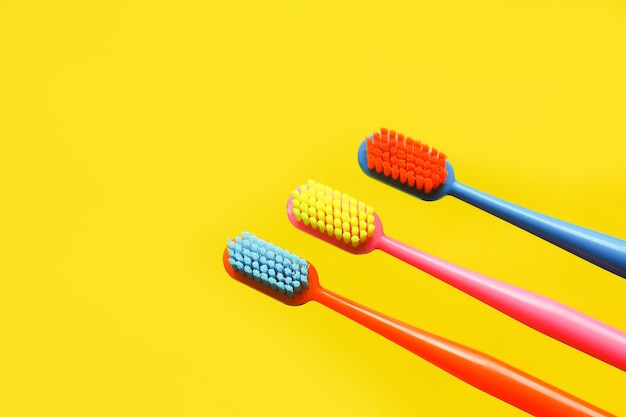 Tre spazzolini da denti multicolori e una statuetta di un dente su sfondo giallo. concetto di pubblicità di odontoiatria. copia spazio.