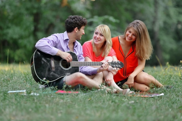 Tre studenti con una chitarra seduti sull'erba nel parco cittadino