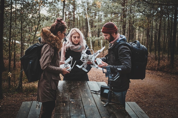 Tre studenti stanno riparando un drone rotto usando il tavolo al parco forestale autunnale.