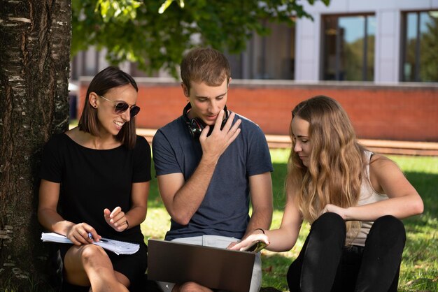 Tre studenti universitari che lavorano insieme su un laptop sotto un albero nel parco del campus