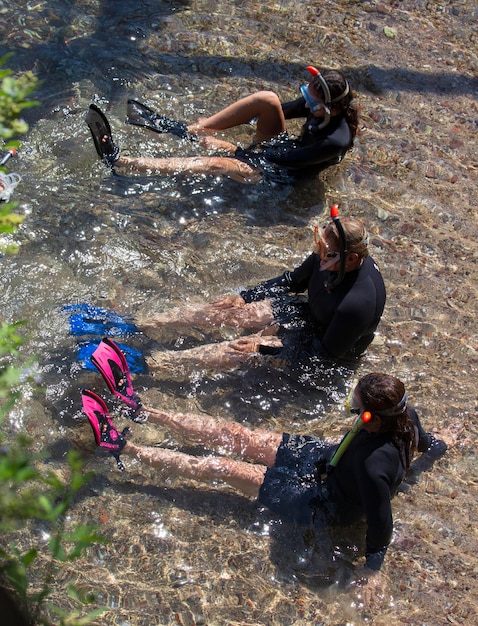 Tre subacquei femminili con maschere subacquee seduti in acque poco profonde che indossano le pinne per nuotare si preparano a tuffarsi nel Mar Rosso I subacquei si siedono sulla riva e indossano pinne da sub e una maschera