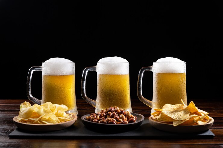 Tre tazze e piatti di birra ghiacciati con gli aperitivi sulla tavola di legno