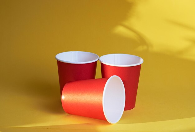 Tre tazze rosse brillanti usa e getta su uno sfondo giallo