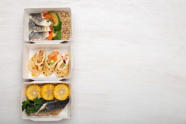 Tre tipi di contenitori per il pranzo con pesce e verdure giacciono su un tavolo bianco. Spazio per la pubblicità. Concetto di mangiare sano.