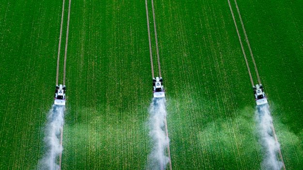 Tre trattori spruzzano pesticidi su una vista dall'alto di un campo verde