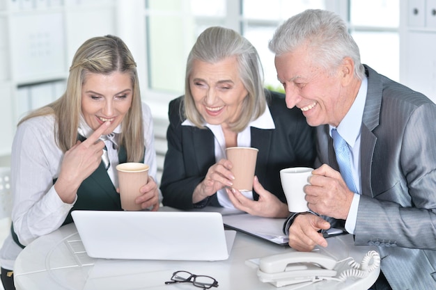 Tre uomini d'affari maturi che usano il laptop e bevono caffè