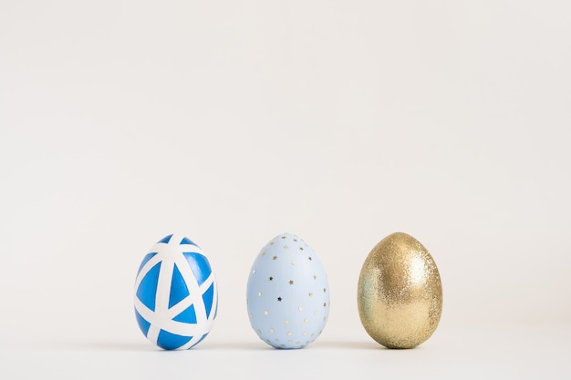 Tre uova decorate dorate di Pasqua su superficie blu. Minimo concetto di Pasqua.