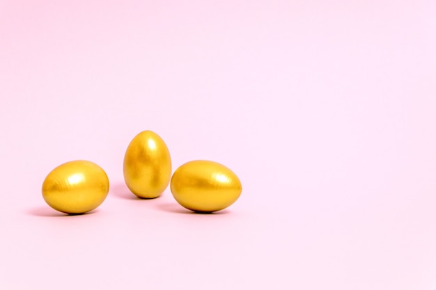 Tre uova di Pasqua decorate con vernice dorata su sfondo rosa. Concetto per Pasqua, primavera. Messa a fuoco selettiva. Copia spazio.