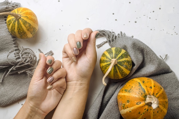 Trend manicure in colori autunnali su un tavolo grigio accanto a zucche e una sciarpa grigia