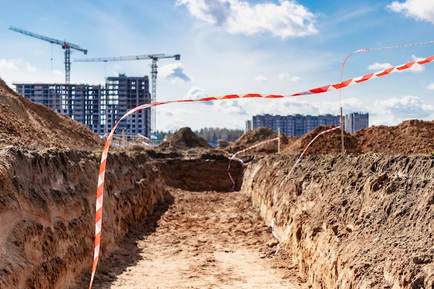 Trincee in cantiere Posa di pozzi e condotte fognarie in calcestruzzo Sistema di drenaggio delle acque reflue per un edificio multipiano Gru a torre in azione Gru per edilizia