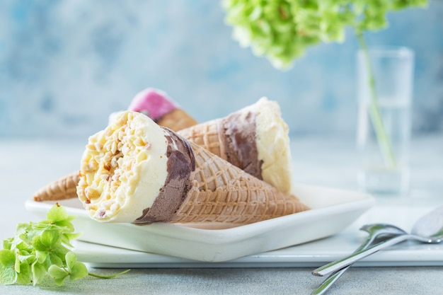 Trio di gustosi coni gelato alla vaniglia e fragola congelati al gusto di dessert con menta su una pietra