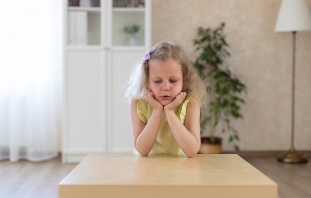 Triste bambina è seduta al tavolo e guardando in basso