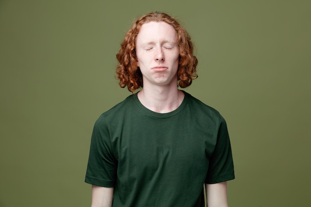 Triste con gli occhi chiusi giovane bel ragazzo che indossa una maglietta verde isolata su sfondo verde