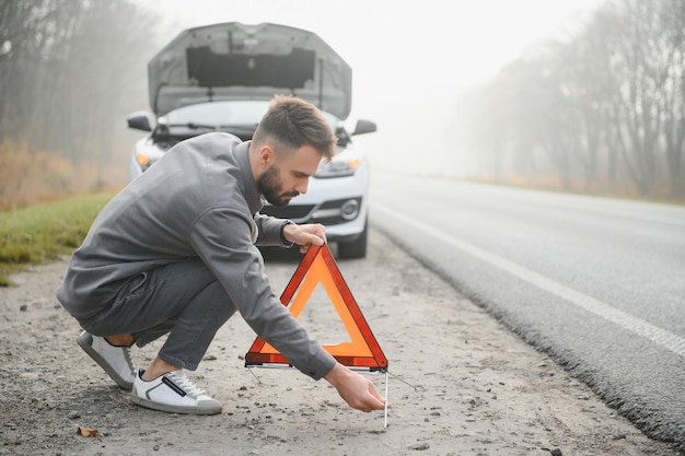 Triste conducente che ha problemi al motore in piedi vicino a un'auto rotta sulla strada Concetto di guasto dell'auto