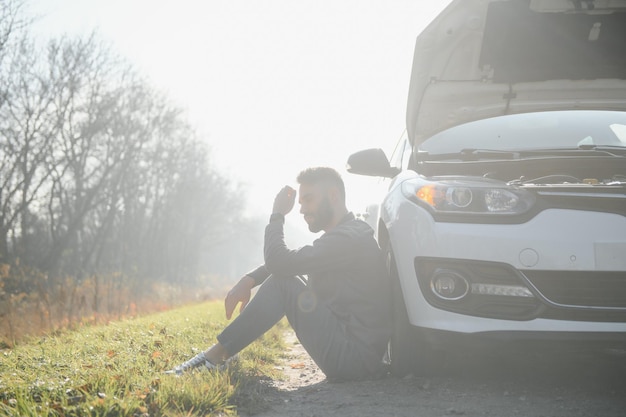 Triste conducente che tiene la testa con problemi al motore in piedi vicino a un'auto rotta sulla strada Concetto di guasto dell'auto