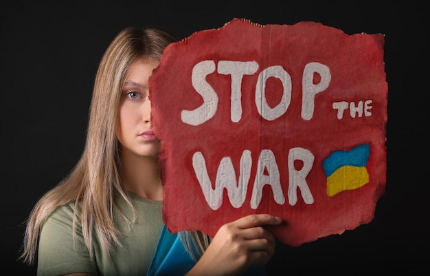 Triste donna che tiene il poster con le parole Stop the War su sfondo nero