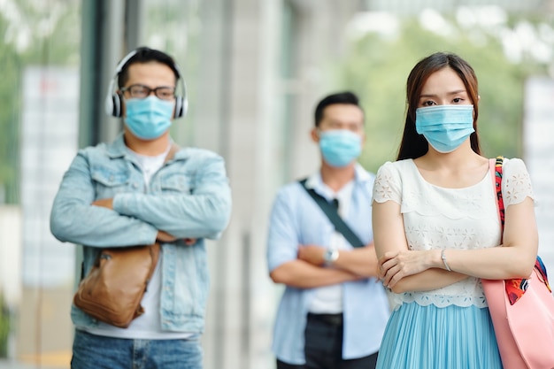 Triste giovane donna asiatica seria in piedi per strada con una maschera medica sul viso